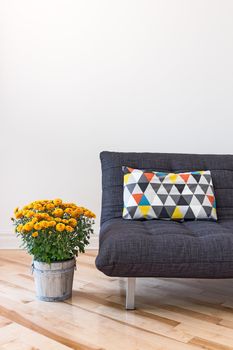 Orange chrysanthemums and gray sofa decorated with bright cushion.