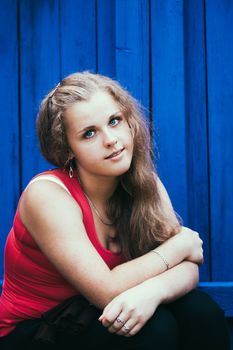 Casual Young Blue-Eyed Girl Sitting Near Blue Wooden Wall