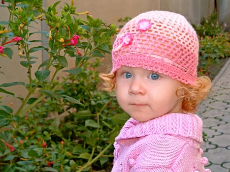 Pensive child with blue eyes around flower beds