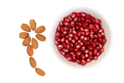Wet pomegrenate seeds in a bowl and flower shaped almonds are next to it, isolated on white