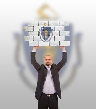 Businessman holding a large piece of a brick wall, flag of Massachusetts, isolated on national flag