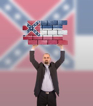 Businessman holding a large piece of a brick wall, flag of Mississippi, isolated on national flag