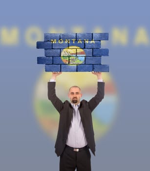 Businessman holding a large piece of a brick wall, flag of Montana, isolated on national flag