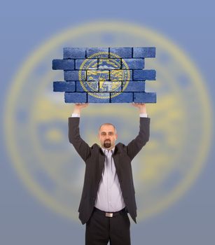 Businessman holding a large piece of a brick wall, flag of Nebraska, isolated on national flag