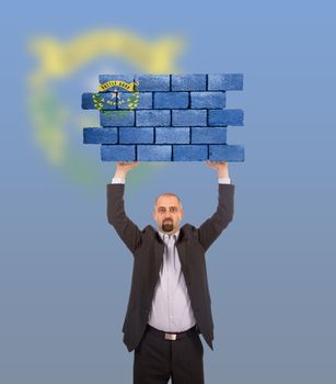 Businessman holding a large piece of a brick wall, flag of Nevada, isolated on national flag