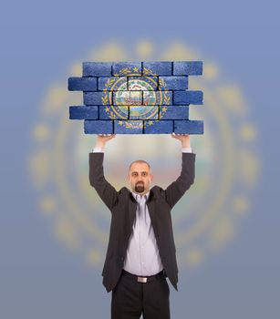 Businessman holding a large piece of a brick wall, flag of New Hampshire, isolated on national flag