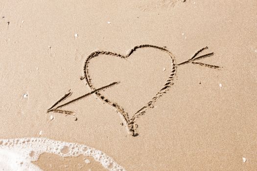 heart with an arrow written on the sandy beach with wave