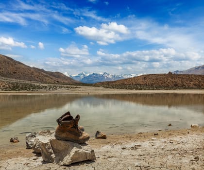 Mountain trekking concept background - trekking hiking boots at mountain lake in Himalayas