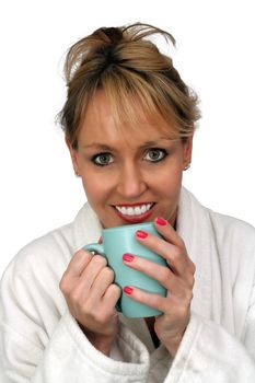 A lovely blonde with a captivating smile and wearing a white bathrobe, enjoys a hot beverage.  Isolated on a white background.