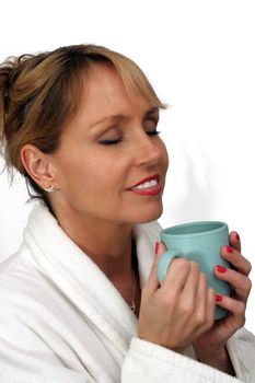 A lovely blonde with a captivating smile and wearing a white bathrobe, enjoys a hot beverage.  Isolated on a white background.