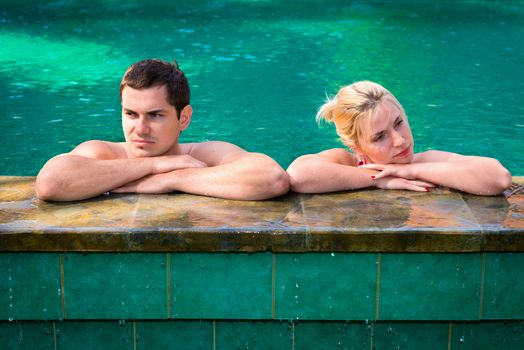 Quarrel in vacation: angry and exasperated young couple in a swimming pool on a poolside in tropical resort