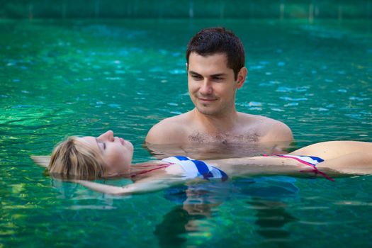 Happy smiling young couple relaxing in a swimming pool in tropical resort