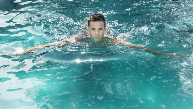An image of a handsome young man swimming in a pool
