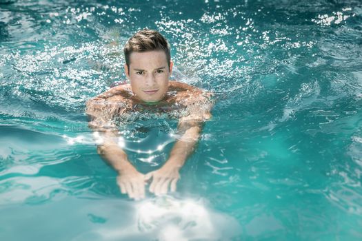 An image of a handsome young man swimming in a pool