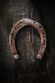 Old worn and rusty horseshoe on wooden background.