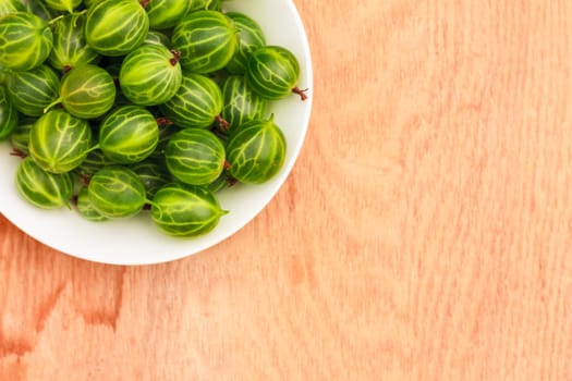 White Dish Filled With Succulent Juicy Fresh Ripe Green Gooseberries On An Old Wooden Table Top.