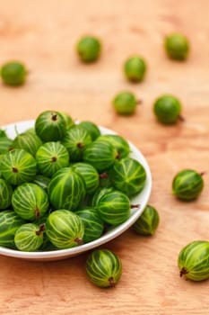 White Dish Filled With Succulent Juicy Fresh Ripe Green Gooseberries On An Old Wooden Table Top.