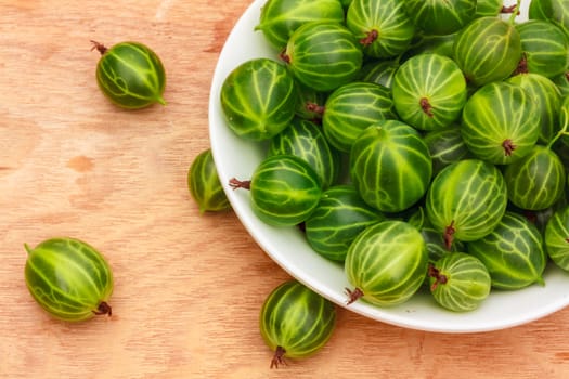 White Dish Filled With Succulent Juicy Fresh Ripe Green Gooseberries On An Old Wooden Table Top.