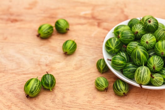 White Dish Filled With Succulent Juicy Fresh Ripe Green Gooseberries On An Old Wooden Table Top.