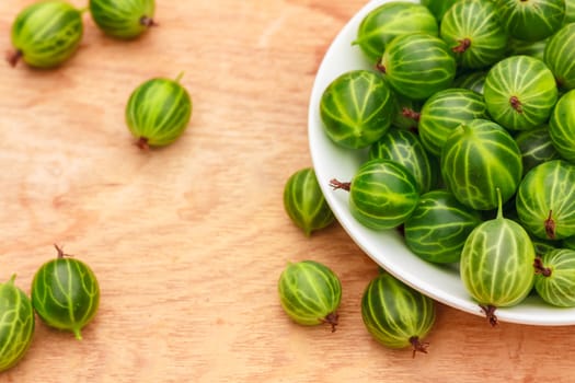 White Dish Filled With Succulent Juicy Fresh Ripe Green Gooseberries On An Old Wooden Table Top.