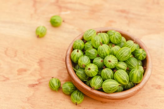 Old Wooden Bowl Filled With Succulent Juicy Fresh Ripe Green Gooseberries On An Old Wooden Table Top.