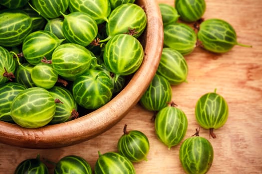 Old Wooden Bowl Filled With Succulent Juicy Fresh Ripe Green Gooseberries On An Old Wooden Table Top.