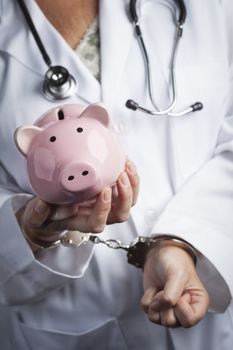 Female Doctor or Nurse In Handcuffs Holding Piggy Bank Wearing Lab Coat and Stethoscope.