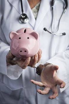 Female Doctor or Nurse In Handcuffs Holding Piggy Bank Wearing Lab Coat and Stethoscope.