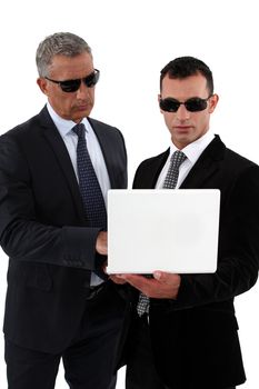 Businessmen wearing sunglasses and looking at a laptop