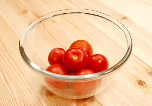 Fresh red tomatoes in a glass bowl, on a wooden table