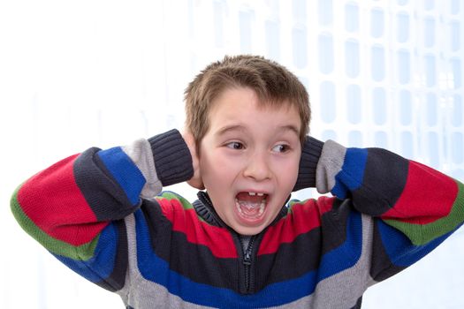 Eight Years old young boy screams with his hands on his ears, perhaps he has some issues