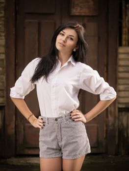 Fashion pretty young woman posing outdoor near a old wooden wall. Beautiful brunette with sensual lips.