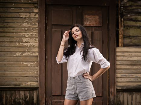 Fashion pretty young woman posing outdoor near a old wooden wall. Beautiful brunette with sensual lips.