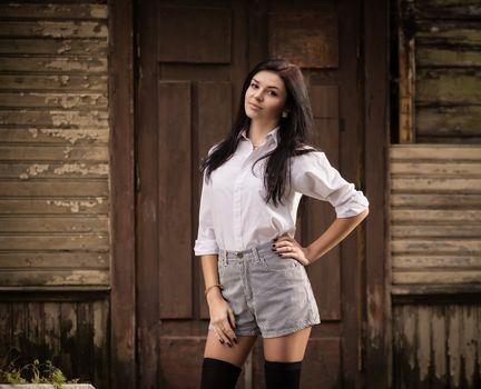 Fashion pretty young woman posing outdoor near a old wooden wall. Beautiful brunette with sensual lips.
