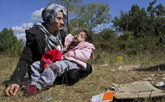 Unknown Syrian mother, holding her sick child is sitting on the grass near a refugee camp in Sofia.