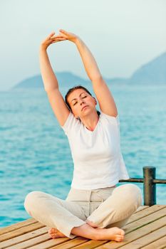 beautiful woman stretching in the morning while sitting on a pier at the sea