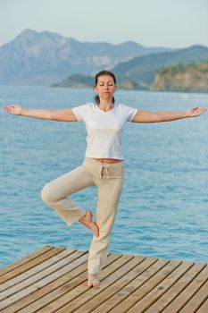 girl by holding a balance while standing on one leg on pier