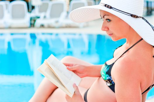 girl in bikini reading a book near the pool