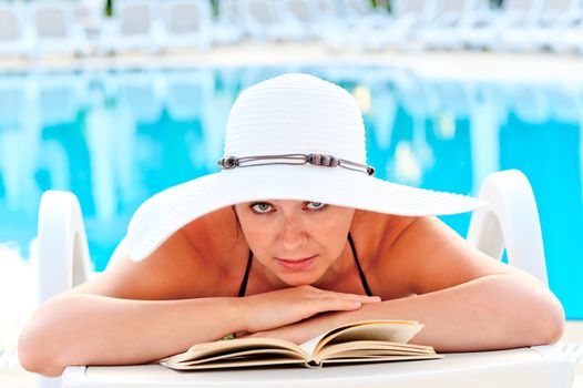 beautiful girl look in a white hat on a sun lounger beside the pool