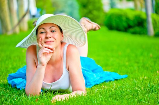 girl lies on a green lawn in a white hat