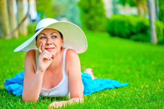 thoughtful girl lies on a green lawn in a white hat