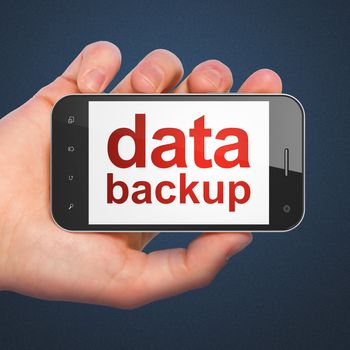 Information concept: hand holding smartphone with word Data Backup on display. Generic mobile smart phone in hand on Dark Blue background.