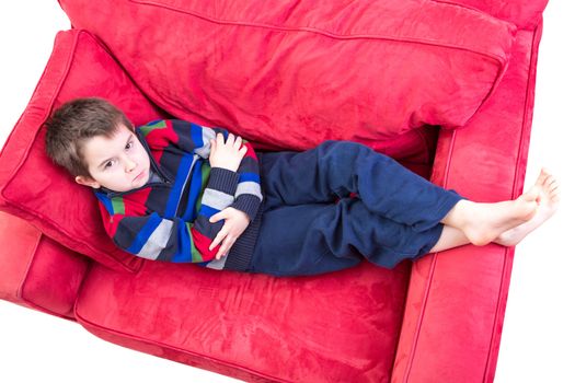 Eight years old boy expression mischievousness with arms closed on the couch by looking up in to your eyes, isolated on white