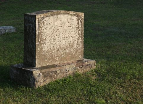 A large gravestone in a graveyard, shot in the golden light of dusk.
