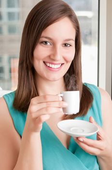 Young woman drinking a hot coffee from a white cup in an office