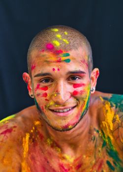 Handsome young man with skin all painted with colors looking in camera smiling