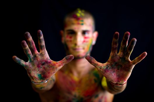 Attractive young man showing all colored hands in foreground. All skin is painted with colors