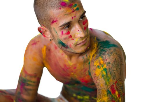 Handsome young man with skin all painted with colors sitting on the floor, isolated on white