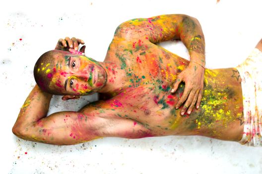 Handsome young man with skin all painted with colors lying on the floor, looking up