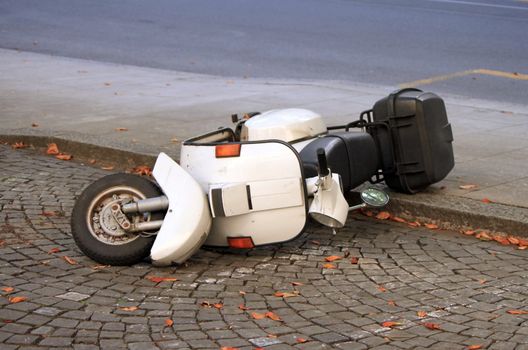 White scooter lying down on pavement in the street